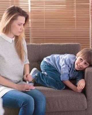 mother looking at her son crawling across the couch with a sneaky grin on his face