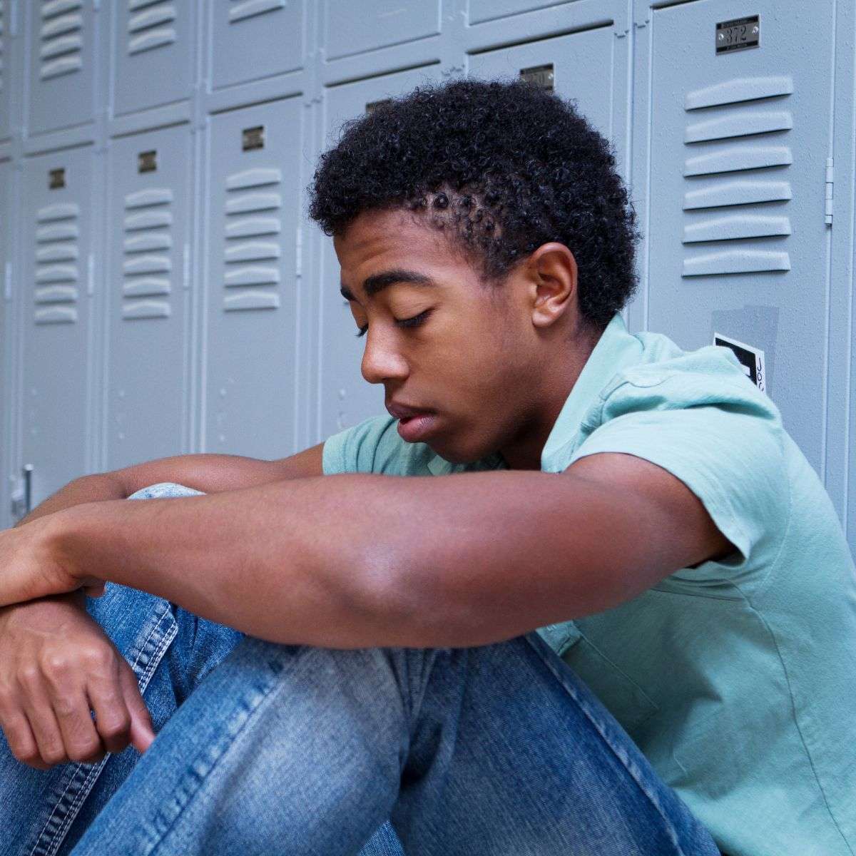 Mindful Healing Adolescent Therapy in New Jersey young african amerian teen boy, looking sad, sitting in front of a row of lockers