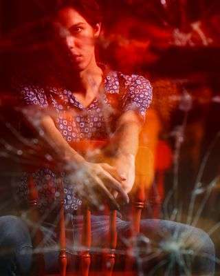 young man sitting in a chair looking back at his reflection in a broken mirror