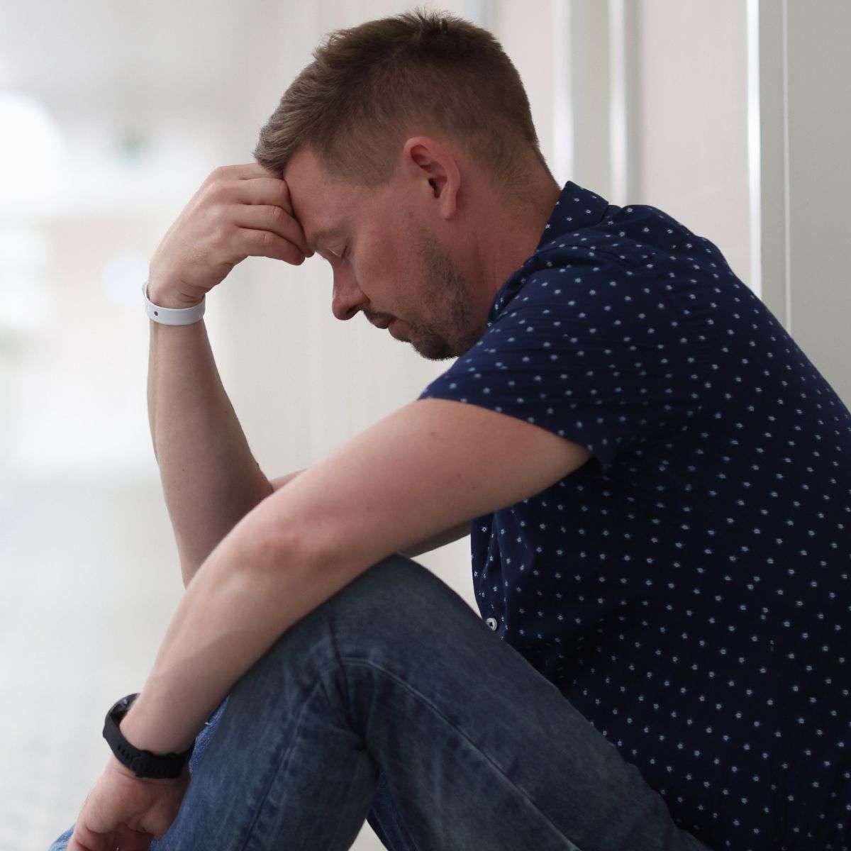Mindful Healing Depression Treatment in New Jersey man sitting with his knees up and his head in his hand, with a hospital bracelet on