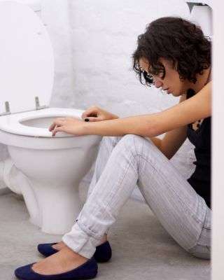 young woman sitting on the ground in front of a toilet looking like she is about to throw up from bulimia