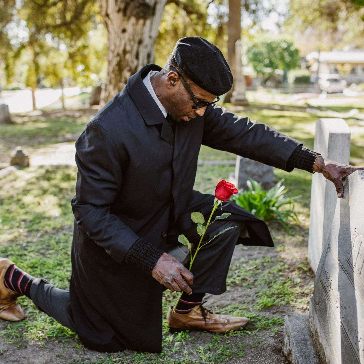 Mindful Healing Grief Counseling in New Jersey african american man kneeling and putting a rose on a tombstone of a loved one