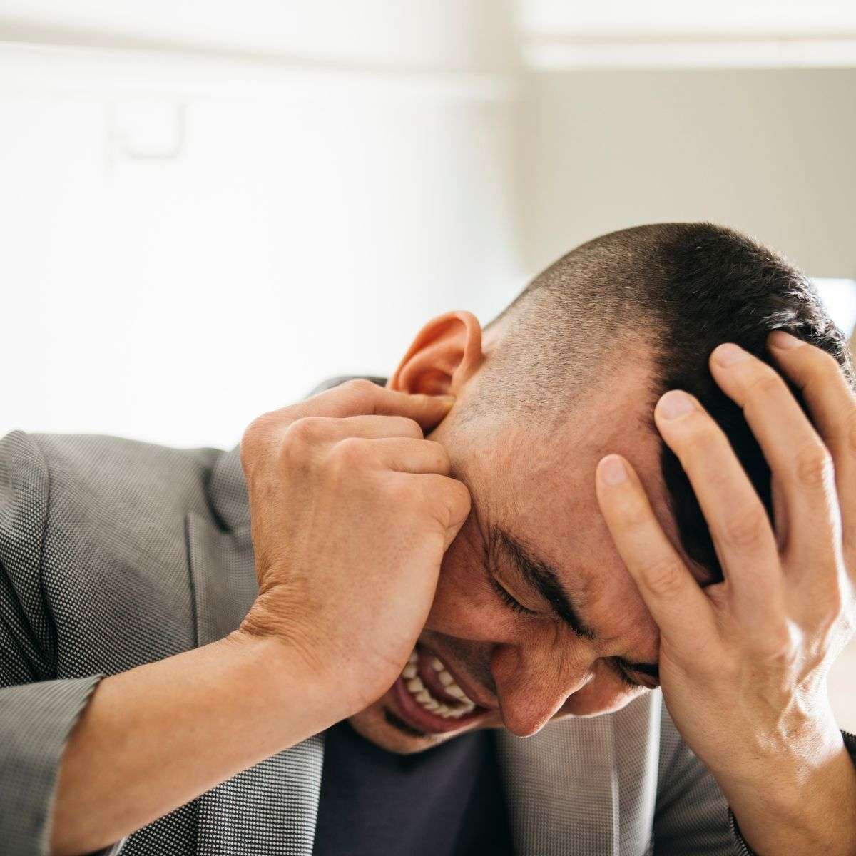 Mindful Healing Schizophrenia Treatment in New Jersey Caucasian man holding his head and plugging his ear like he's trying to stop hearing voices