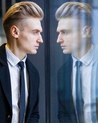 Man looking out a window and his reflection looking back